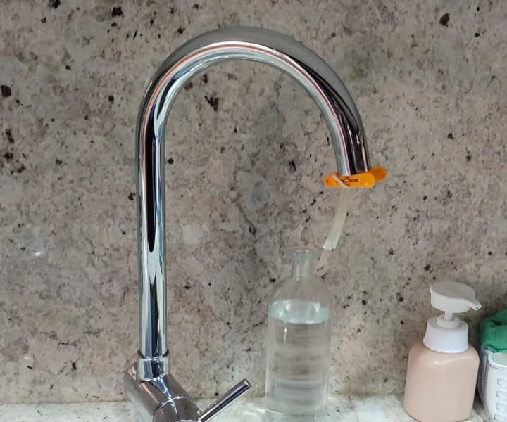 Aixeta de cuina amb un filtre d’aigua instal·lat a la sortida i una ampolla d’aigua filtrada al costat.