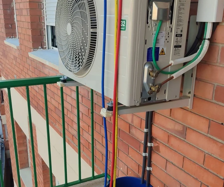 Unitat exterior connectada al quadre elèctric, amb el cablejat i les línies frigorífiques a la vista.